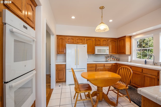 kitchen with white appliances, light tile patterned floors, brown cabinets, decorative light fixtures, and a sink