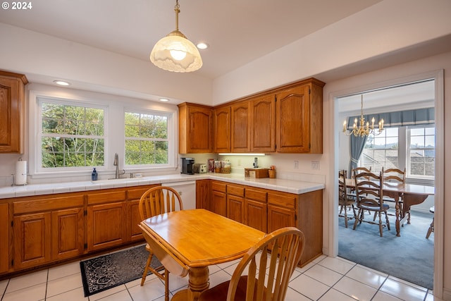 kitchen with light countertops, brown cabinets, dishwasher, and a notable chandelier