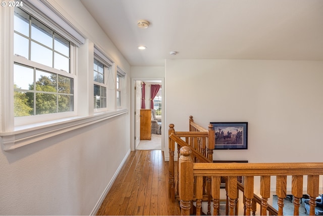 hall featuring recessed lighting, wood-type flooring, baseboards, and an upstairs landing