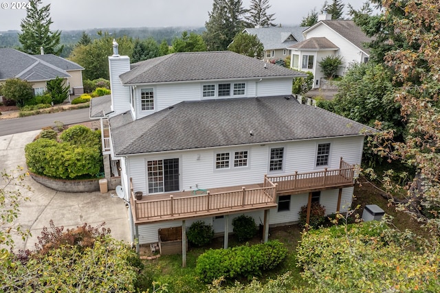 rear view of property with a deck, a shingled roof, and a chimney