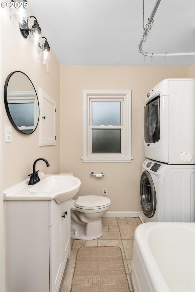 bathroom with stacked washing maching and dryer, a tub, vanity, and toilet