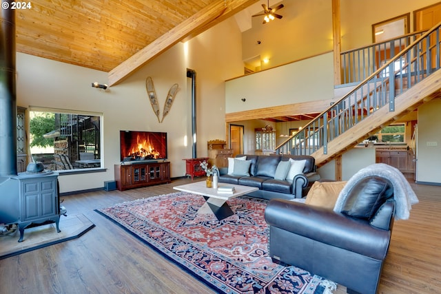 living room featuring wood-type flooring, beamed ceiling, a wood stove, high vaulted ceiling, and wooden ceiling