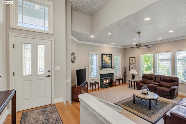 living room with a high end fireplace, a textured ceiling, light hardwood / wood-style flooring, ornamental molding, and ceiling fan