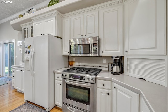 kitchen with ornamental molding, a textured ceiling, white cabinetry, appliances with stainless steel finishes, and light wood-type flooring