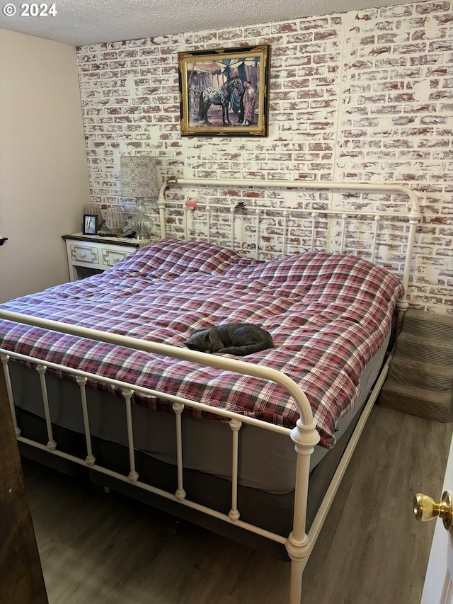 bedroom featuring a textured ceiling, brick wall, and dark hardwood / wood-style floors