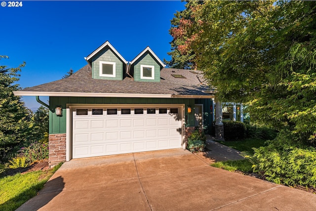 view of front of property with an attached garage, driveway, roof with shingles, and stone siding