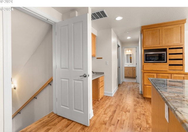 kitchen with light wood-type flooring, light stone countertops, and stainless steel microwave