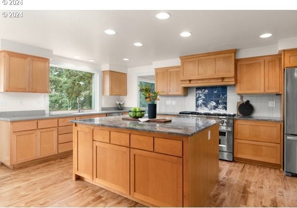 kitchen featuring appliances with stainless steel finishes, stone countertops, light wood-style floors, and a center island