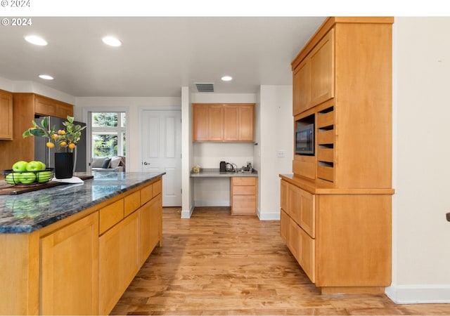 kitchen featuring dark stone countertops, stainless steel refrigerator, black microwave, and light hardwood / wood-style floors