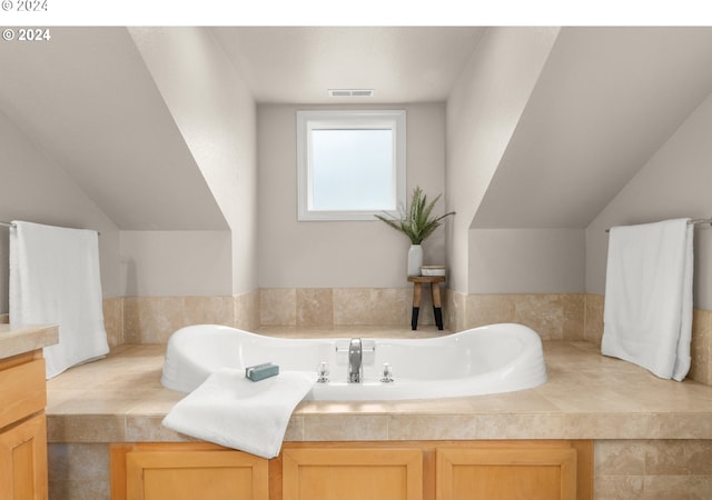 bathroom featuring lofted ceiling, a relaxing tiled tub, and vanity