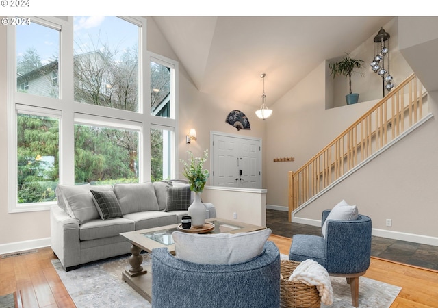 living area with stairs, high vaulted ceiling, wood finished floors, and baseboards