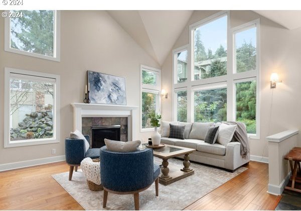 living room featuring light wood-type flooring, baseboards, high vaulted ceiling, and a tile fireplace