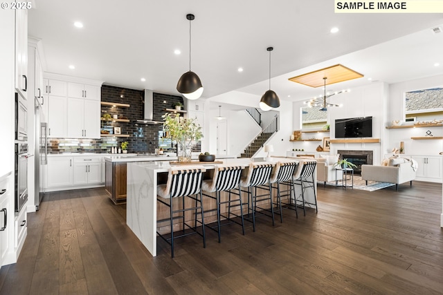 kitchen featuring white cabinetry, dark wood-type flooring, an island with sink, pendant lighting, and a breakfast bar area