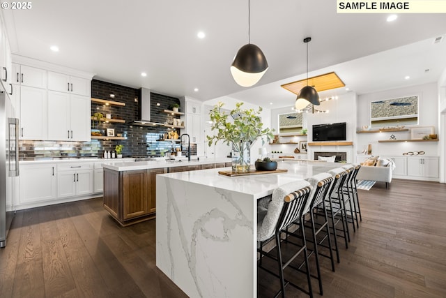 kitchen featuring light stone countertops, a spacious island, pendant lighting, dark hardwood / wood-style floors, and white cabinetry