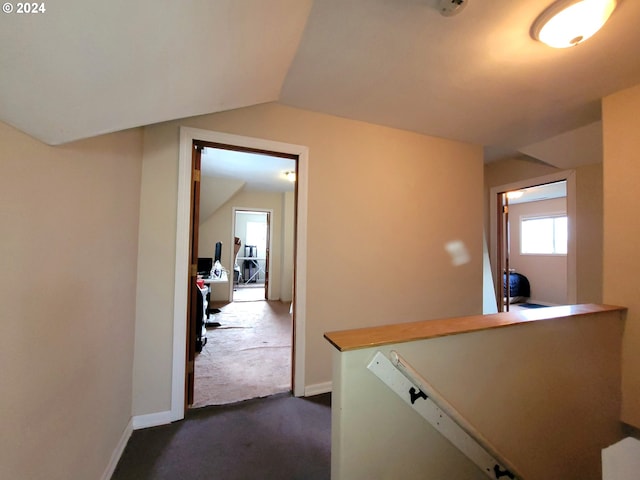 corridor with lofted ceiling and dark colored carpet