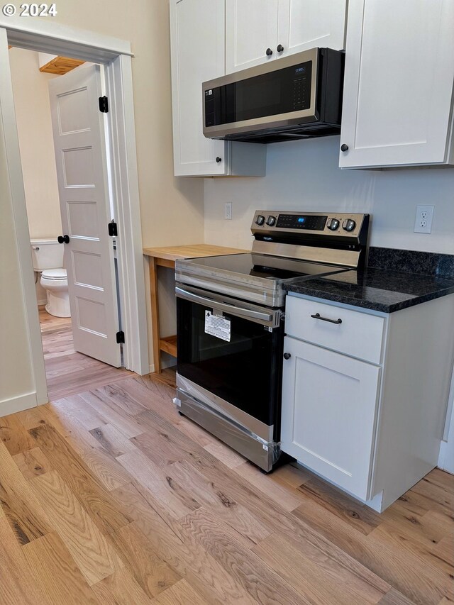 kitchen featuring white cabinets, stainless steel appliances, light hardwood / wood-style floors, and dark stone counters