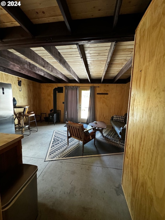 unfurnished living room featuring beamed ceiling, a wood stove, and wooden walls