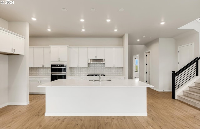 kitchen with white cabinets, a center island with sink, and light countertops