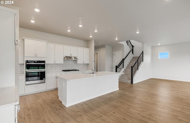 kitchen with a kitchen island with sink, black gas cooktop, decorative backsplash, light hardwood / wood-style floors, and white cabinetry