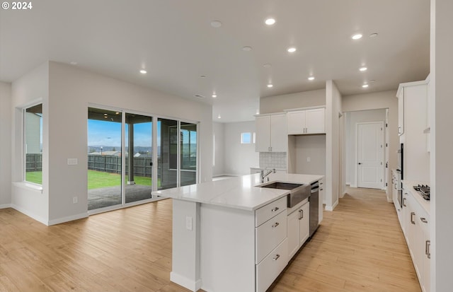 kitchen with light stone counters, a center island with sink, white cabinets, a sink, and dishwasher