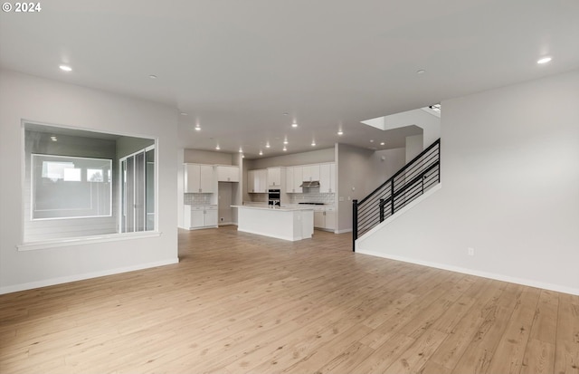 unfurnished living room featuring baseboards, stairway, recessed lighting, and light wood-style floors