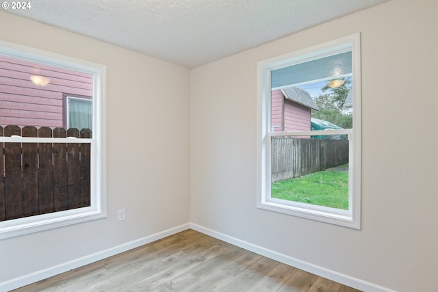 spare room with a textured ceiling, light hardwood / wood-style floors, and a wealth of natural light