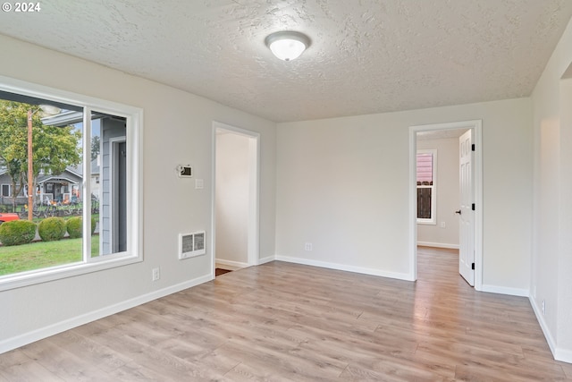 empty room featuring plenty of natural light, light hardwood / wood-style floors, and a textured ceiling