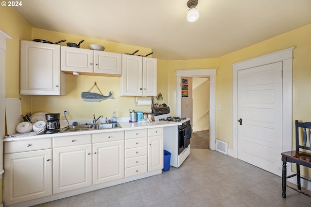 kitchen with white gas range oven, white cabinetry, and sink