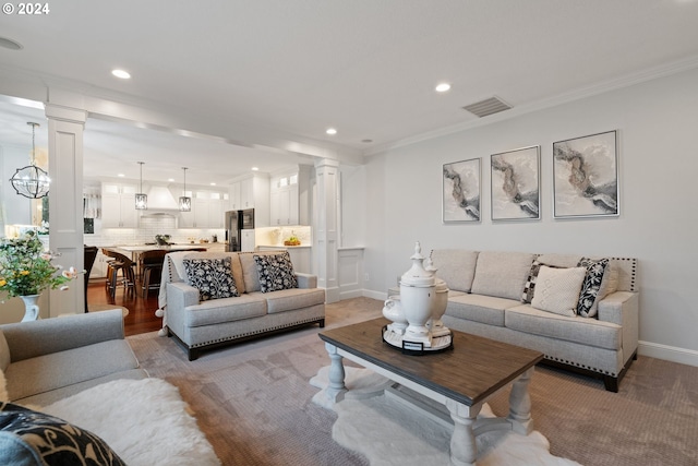 living room featuring a notable chandelier, ornate columns, and crown molding