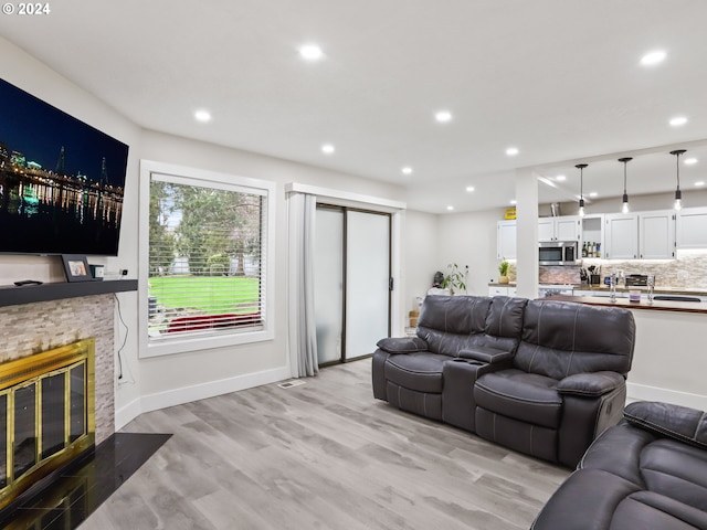 living room with a stone fireplace and light wood-type flooring