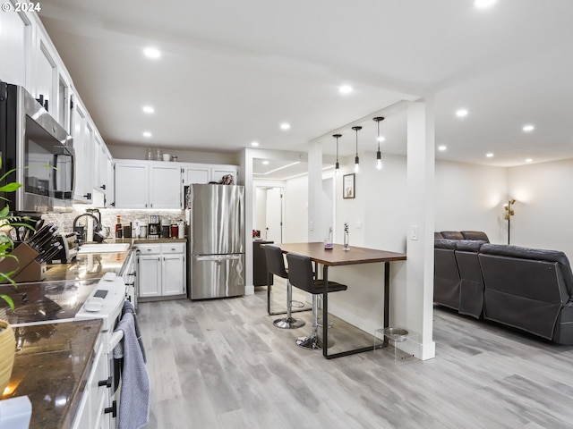 kitchen featuring pendant lighting, white cabinets, backsplash, light hardwood / wood-style floors, and stainless steel appliances