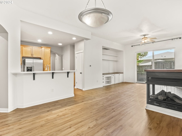 living room featuring light wood-type flooring, ceiling fan, sink, built in features, and a multi sided fireplace