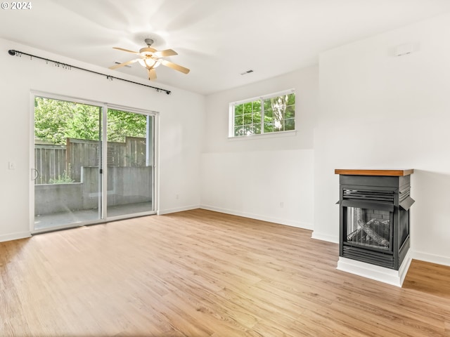 unfurnished living room with a multi sided fireplace, ceiling fan, a healthy amount of sunlight, and light hardwood / wood-style floors