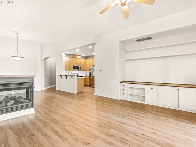 unfurnished living room with ceiling fan, a multi sided fireplace, and light wood-type flooring