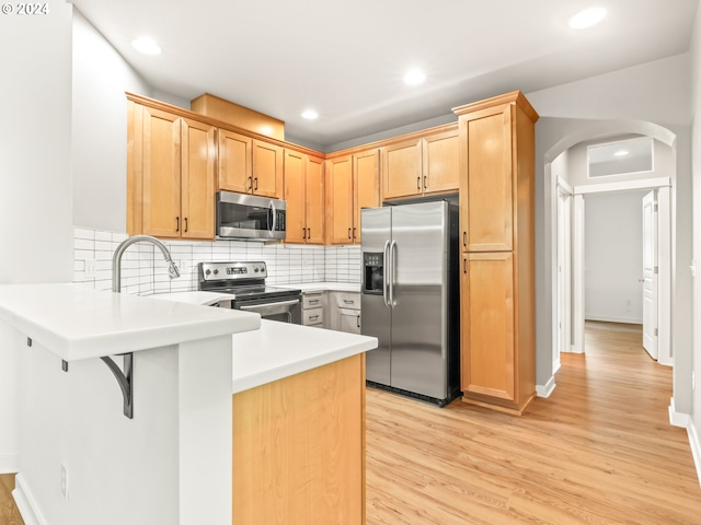 kitchen featuring light hardwood / wood-style flooring, backsplash, kitchen peninsula, light brown cabinetry, and appliances with stainless steel finishes