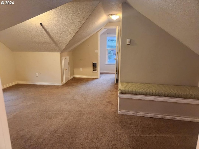 additional living space featuring vaulted ceiling, heating unit, carpet, and a textured ceiling