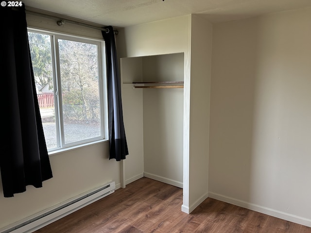 unfurnished bedroom with a closet, dark hardwood / wood-style flooring, and a baseboard heating unit