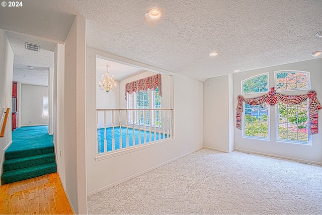 unfurnished room featuring light carpet, a textured ceiling, and an inviting chandelier