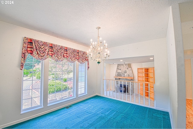 carpeted spare room with a chandelier, built in shelves, a stone fireplace, and a textured ceiling