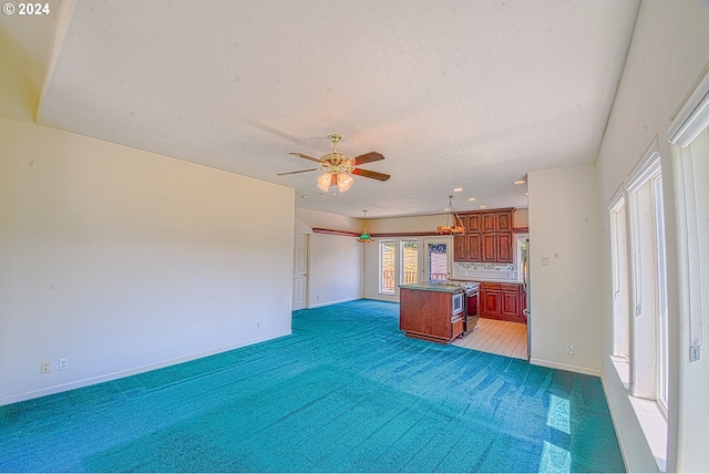 kitchen with dark carpet, stainless steel stove, a textured ceiling, ceiling fan, and a kitchen island