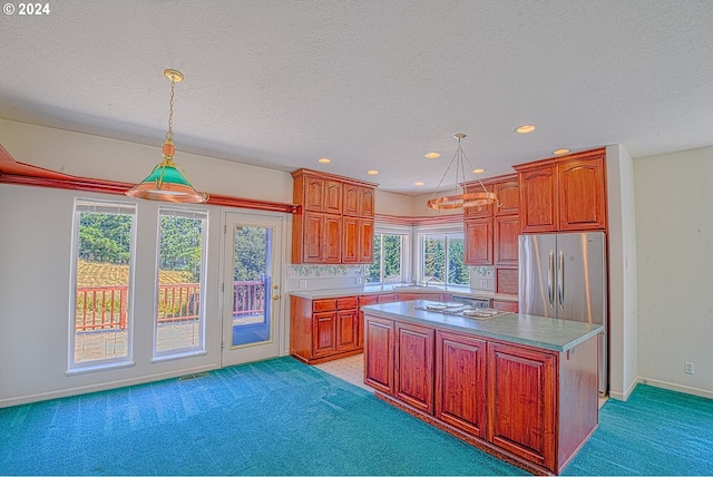 kitchen with carpet floors, a kitchen island, stainless steel refrigerator, sink, and pendant lighting