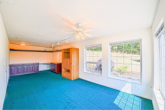 interior space featuring dark colored carpet, built in desk, a textured ceiling, and a healthy amount of sunlight