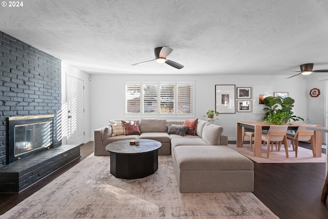 living room with a textured ceiling, ceiling fan, wood-type flooring, and a fireplace