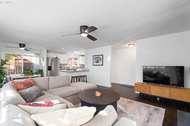 living room with a textured ceiling, ceiling fan, and dark wood-type flooring