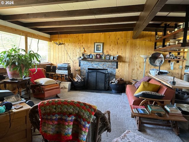 interior space featuring a stone fireplace, wooden walls, carpet floors, and beam ceiling