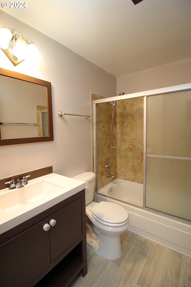 full bathroom featuring vanity, wood-type flooring, bath / shower combo with glass door, and toilet