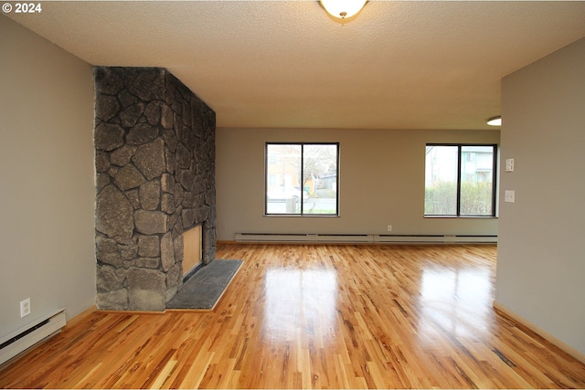 unfurnished living room featuring a baseboard radiator, a healthy amount of sunlight, a textured ceiling, and light wood-type flooring