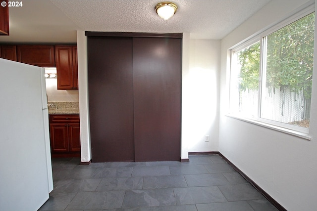 unfurnished bedroom featuring white refrigerator, connected bathroom, a closet, and a textured ceiling