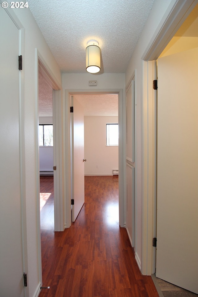 hallway with dark wood-type flooring, a textured ceiling, and a baseboard heating unit