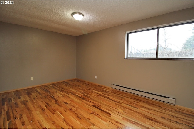 spare room with a baseboard heating unit, a textured ceiling, and light wood-type flooring